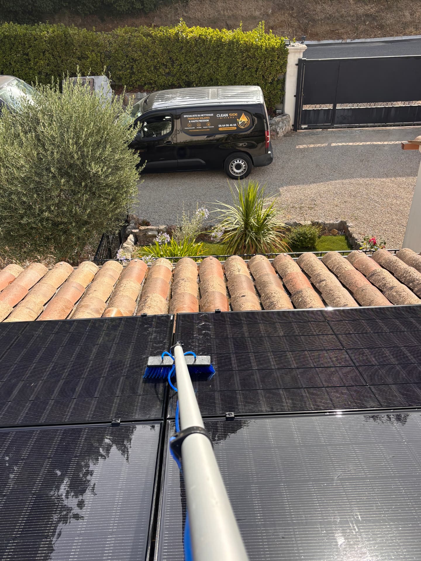 Nettoyage de panneaux solaires à la perche télescopique sur une toiture en tuiles, fourgonnette Clean Side Riviera visible en contrebas